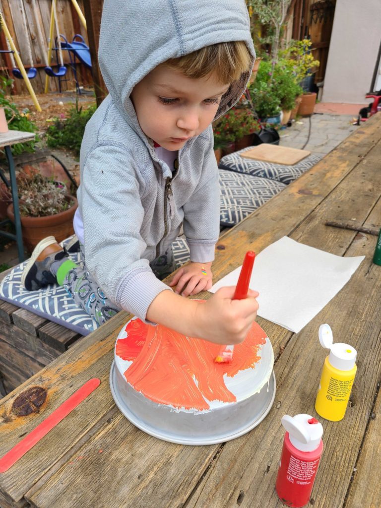 A child brushing orange paint on a pie tin to create a monoprint