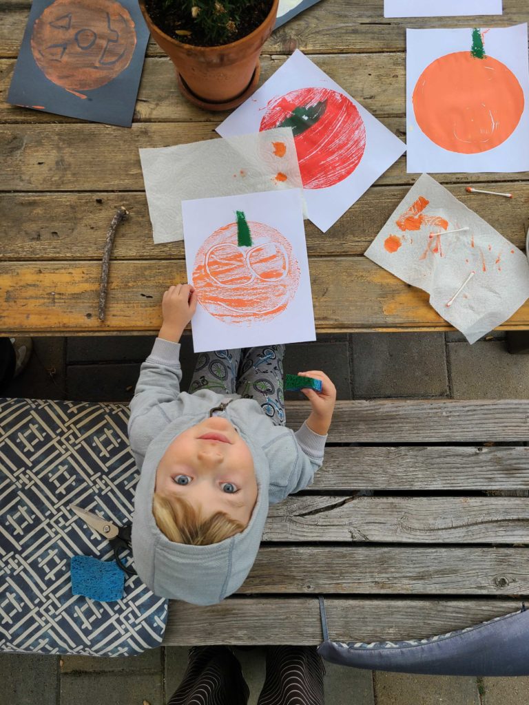 bird's eye view of a child looking up while siting at a wooden table covered in orange pumpking paintings