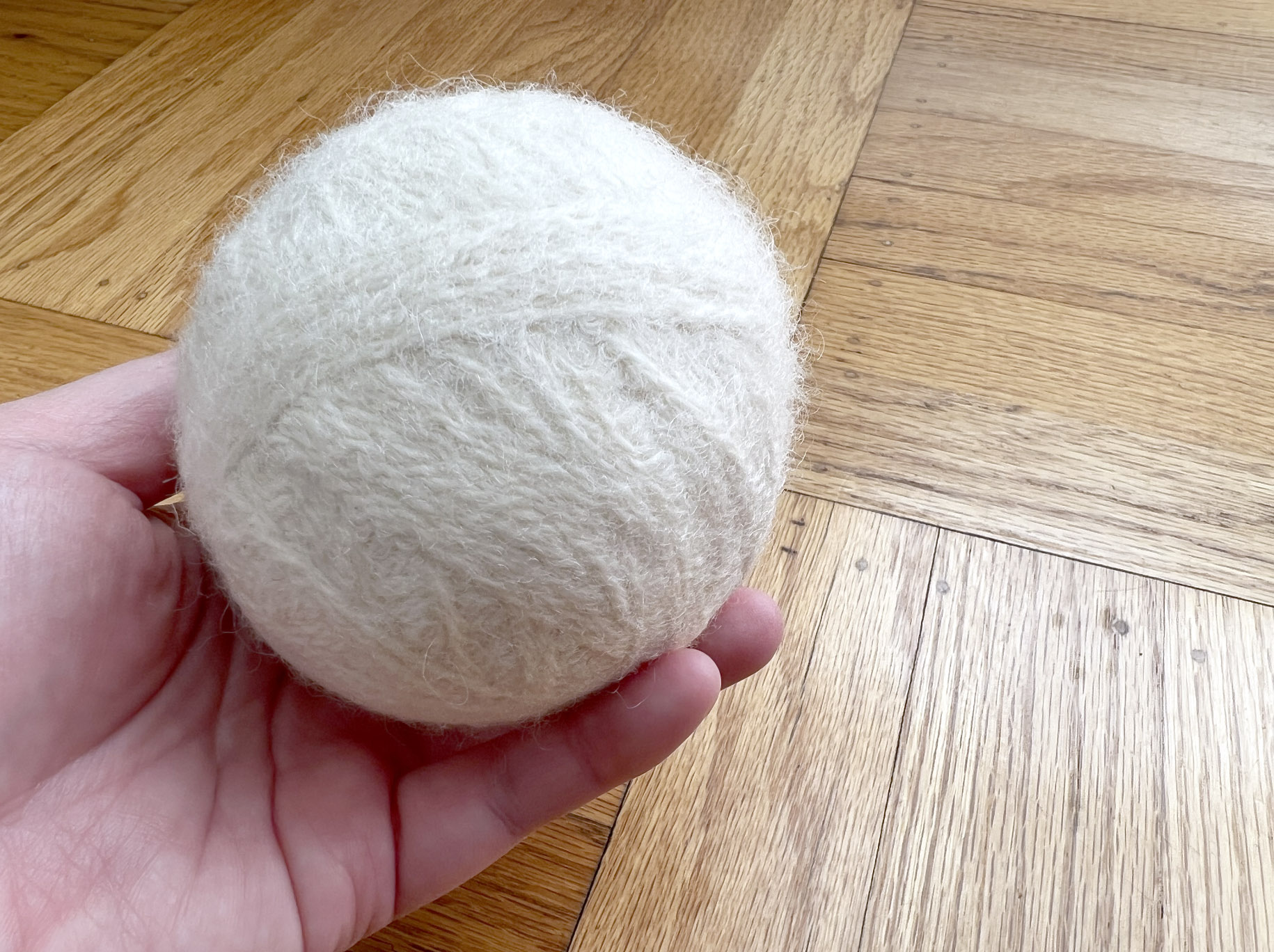 image of hand holding a white felted wool dryer ball