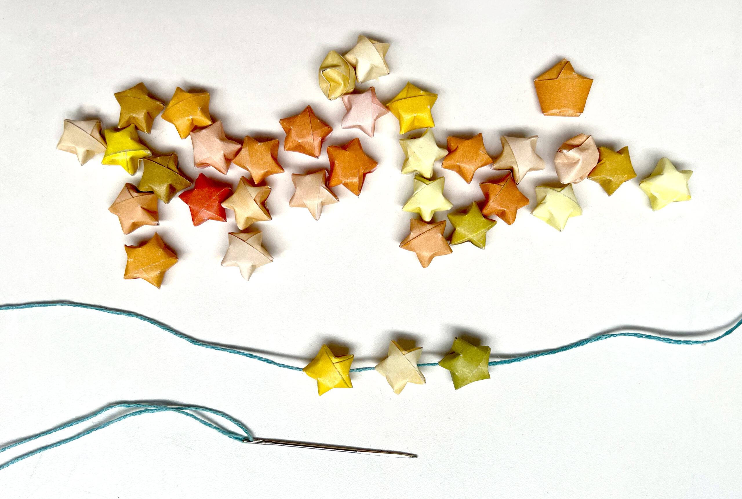 image of a pile of colorful paper stars getting strung together with needle and thread
