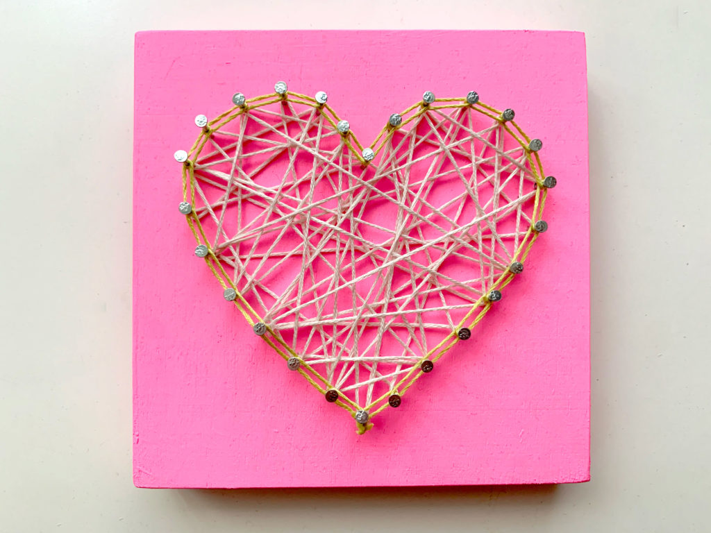 Heart-shaped string art with ecru string and a pink wood board