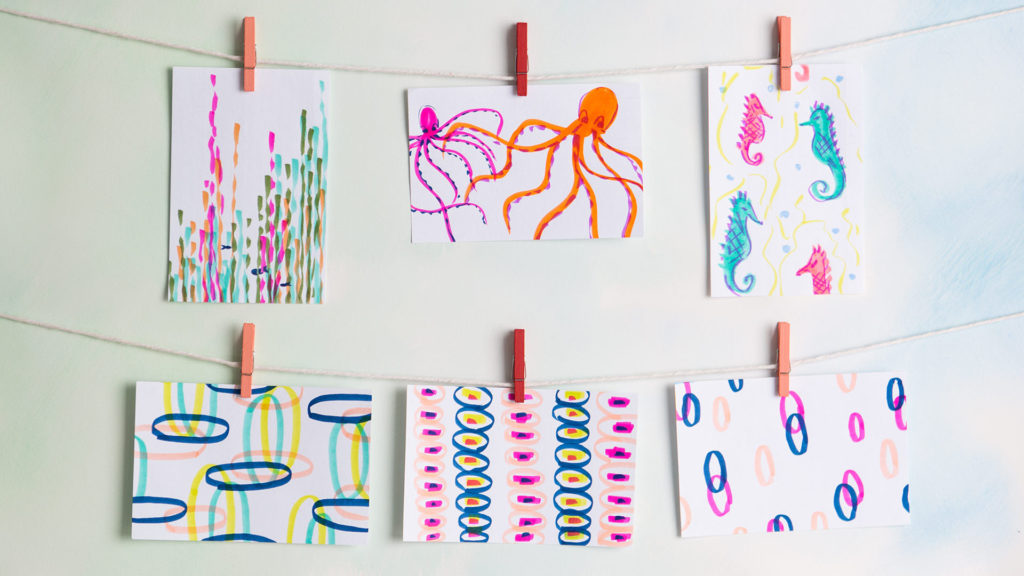 6 different colorful marker drawings strung on string and clothes pins, some depicting circular patterns, some octopi, some seahorses