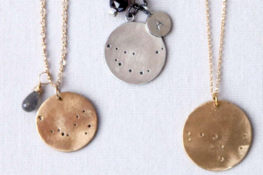 flat lay closeup of 3 metal necklaces with zodiac designs stamped on