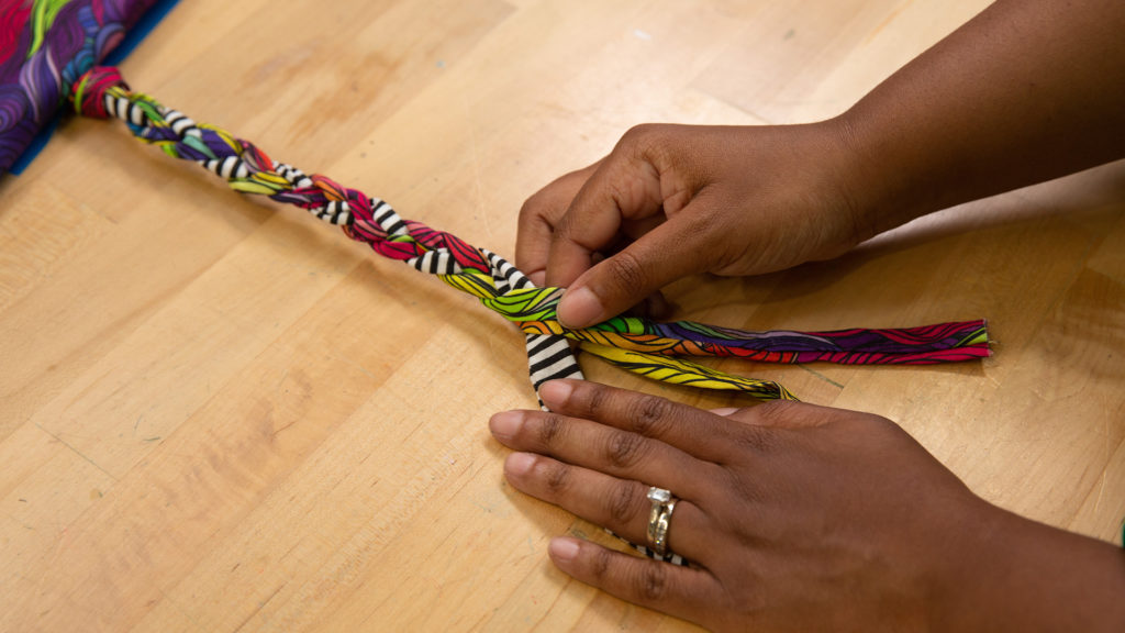 close-up of two hands braiding colorful fabric to sew a necklace