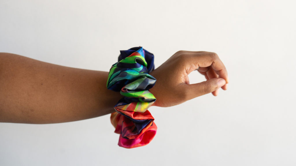 a close-up of an outstretched arm with a vibrant, handmade rainbow fabric scrunchie worn around the wrist