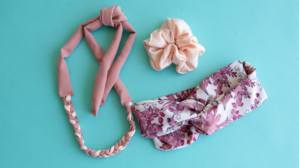 flatlay on light teal background of a braided fabric necklace, scrunchie, and turban headband all sewn with fabric in various soft shades and prints of pink and cream.