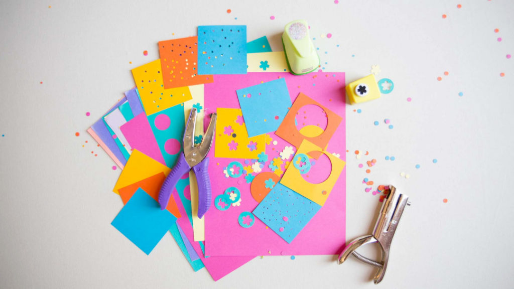 a flat lay of neon colored construction paper and paper punches with lots of punched out confettie