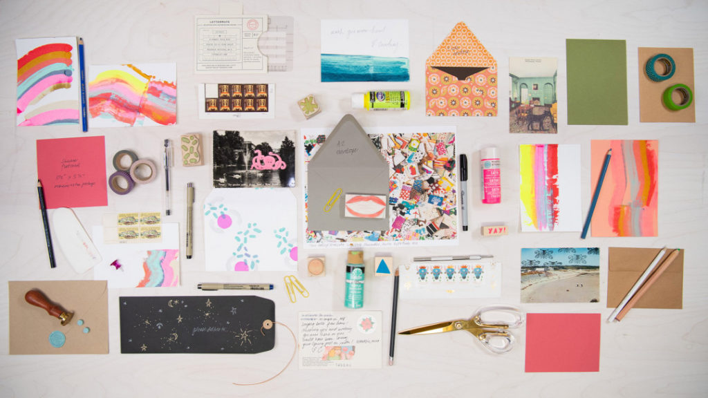 a flat lay of cards, envelopes, paper, pens, washi tape, wax seals, paint and glue for sending creative mail