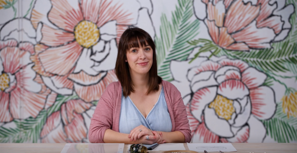 Lauren of Lark Rising sits in front of a large backdrop depicting large graphic flowers in pink, yellow, and green