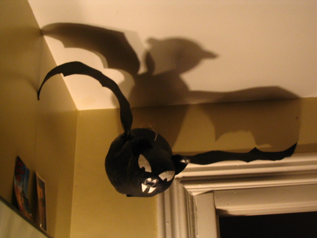 A large black paper mache hat hanging in a dark corner in a home, casting fun shadows on the ceiling