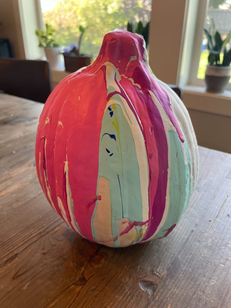 a pumpkin decorated with a paint pouring decorate and several layers of paint in pink, purple, white, and mint green