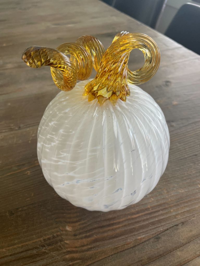 a white and yellow blown glass pumpkin sitting on a wooden table