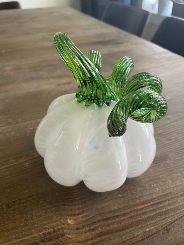 a white and green blown glass pumpkin on a wooden table