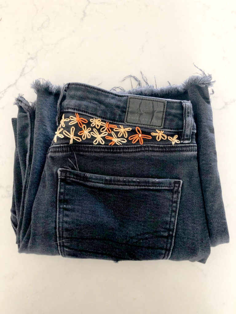 black jeans folded on a table with orange and cream hand embroidered flowers embellishing the top of the waist