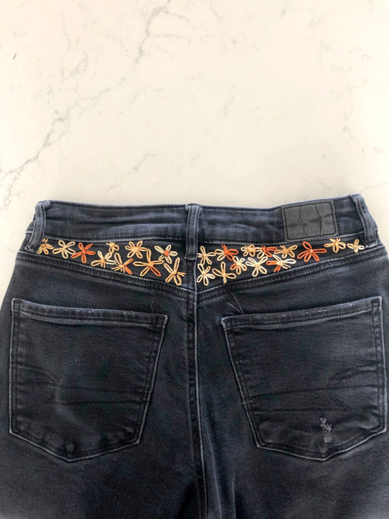 black jeans on a table with orange and cream hand embroidered flowers on the top of the waist