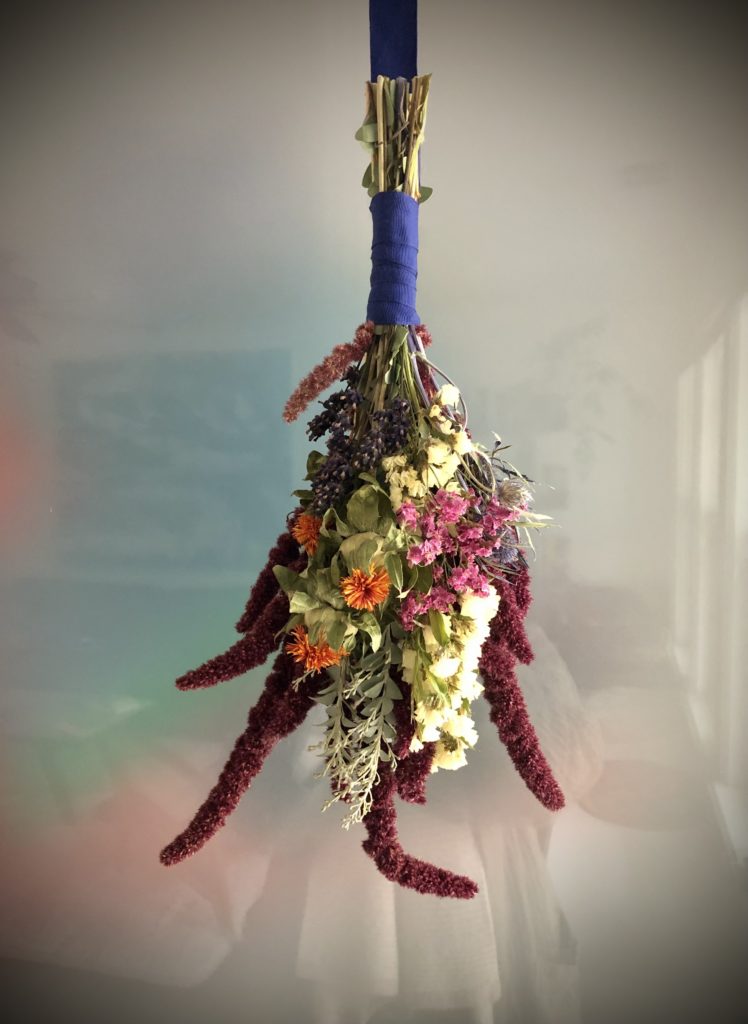 a fresh floower bough hanging upside down, wrapped in purple ribbon
