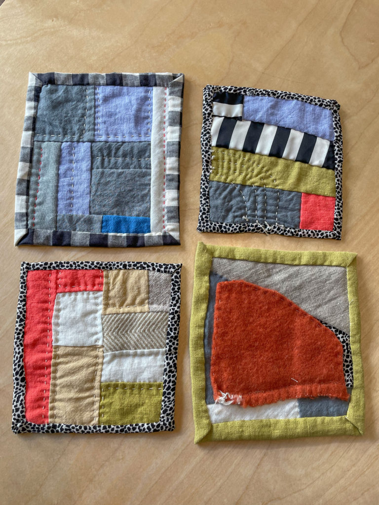 four mini quilts on a table sewn with scraps in different colors and prints
