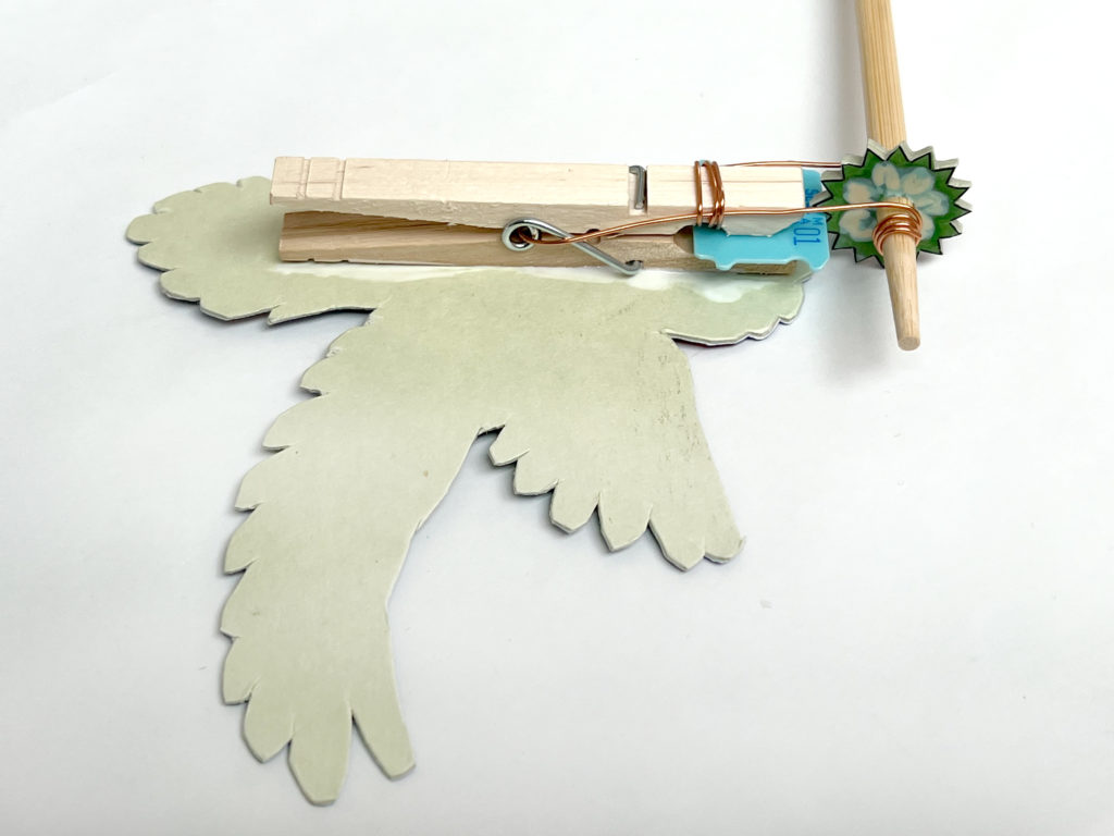 a photo showing the backside of a paper bird and how to glue a DIY noisemaker mechanism to it