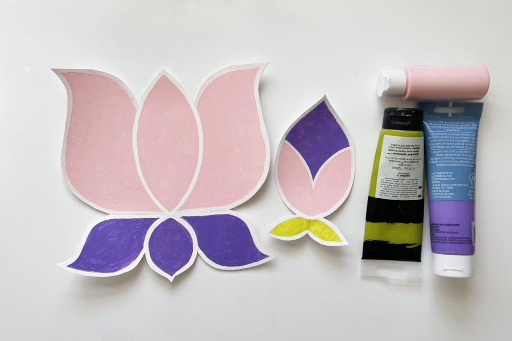 a colorfully painted paper lotus and paper lotus bud, plus pink, green, and purple tubes of acrylic paint, ready for sand art
