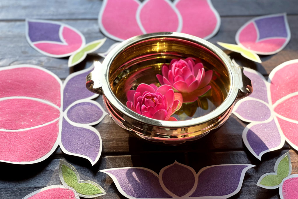 close of up for sand art rangoli and a brass bowl of water and pink blossoms