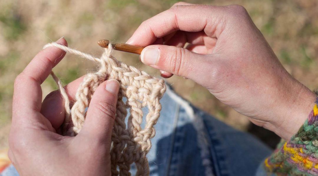 image of instructor Cal Patch's hands crocheting with a wooden hook and ecru colored yarn