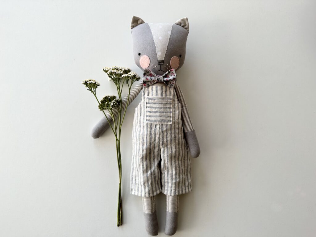 image of cat doll by luckyjuju wearing hand-sewn overalls and bow tie and holding a flower