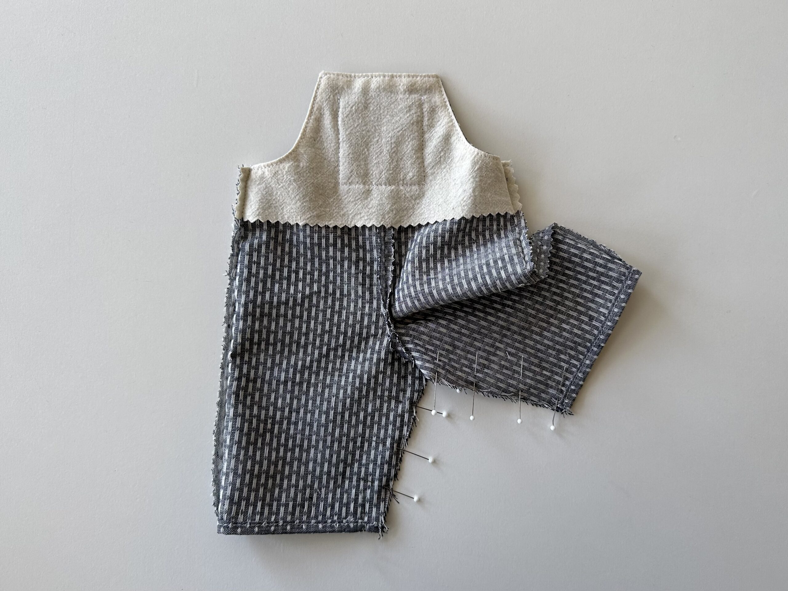 image of doll-sized overalls on a white table with the inseam pinned