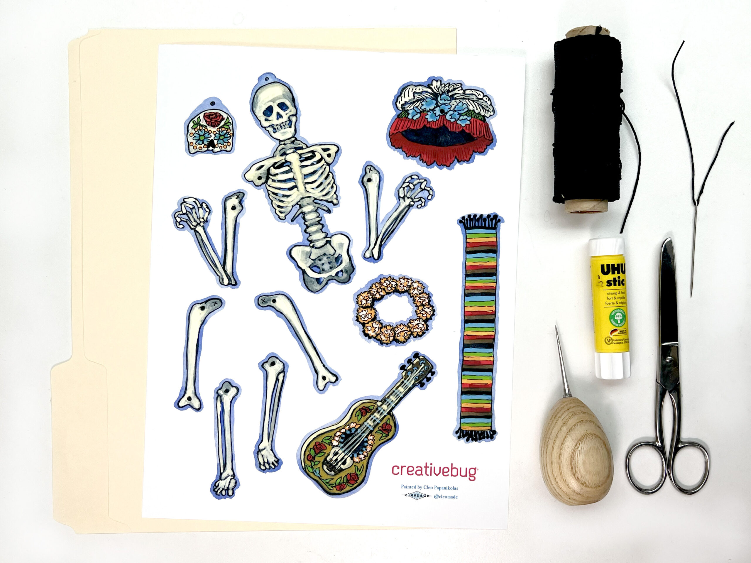 image of materials needed to make a paper skelton including a paper template, twine, scissors, glue stick, and awl