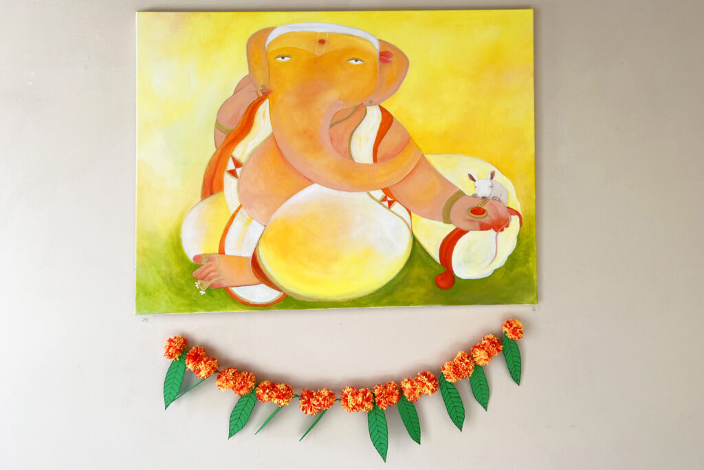 image of a painting of a Hindu elephant god hanging on a wall with a DIY marigold garland strung underneath