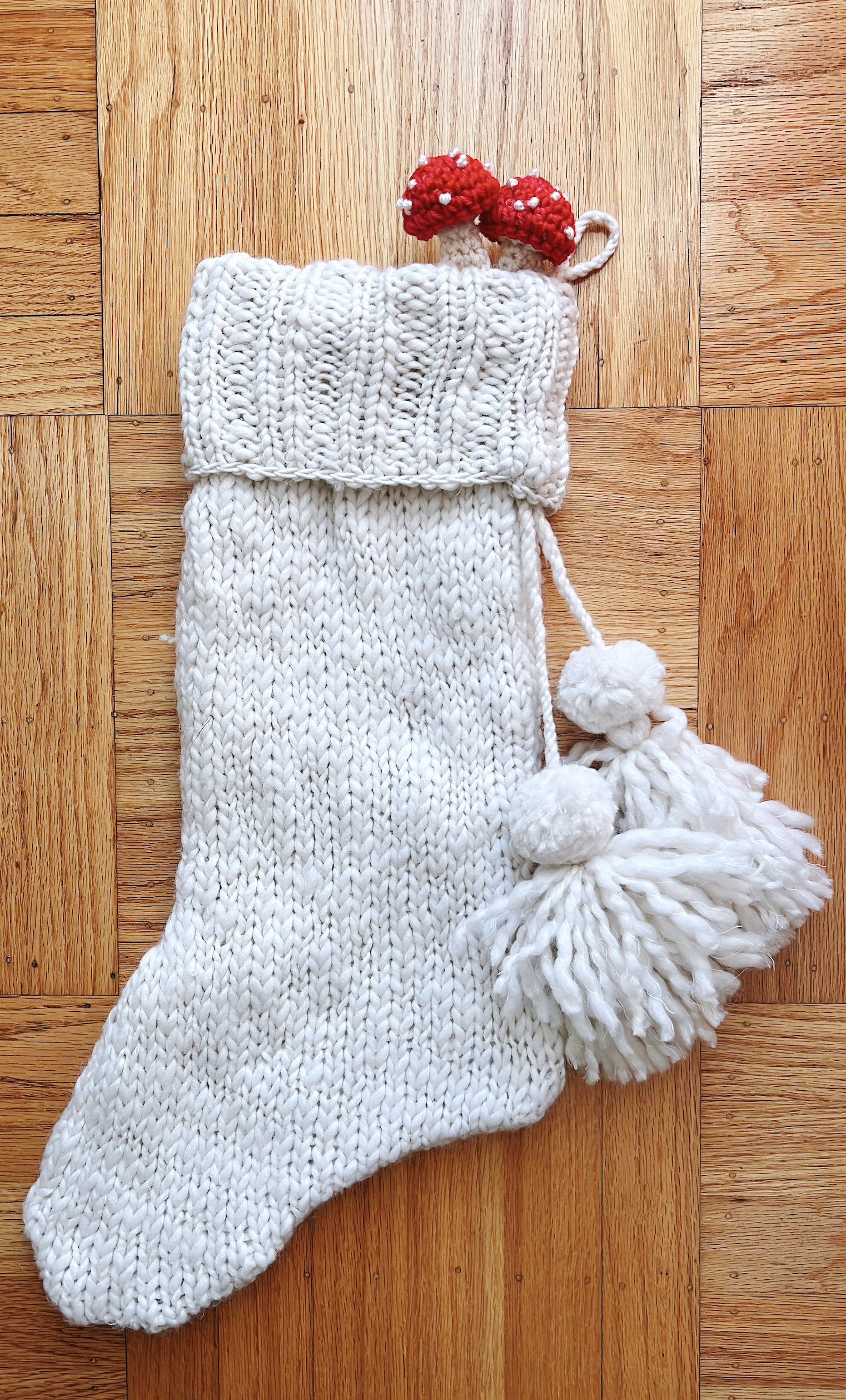 image of white knit stocking with 2 tiny crocheted red and white mushrooms peeking out of the top