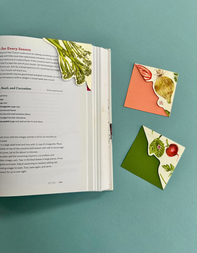 image of open cookbook on blue background and three corner bookbooks made with calendar pages and cardstock with paintings of vegetables