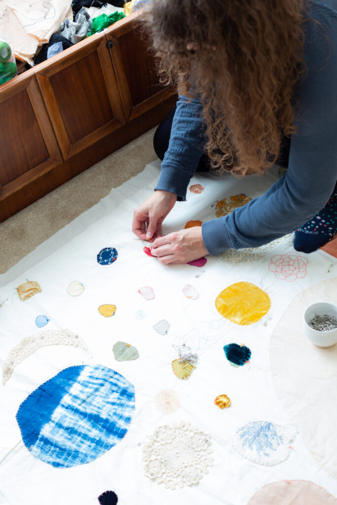 image of a a woman kneeling on a handmade quilt that is on the floor while working on some sewing