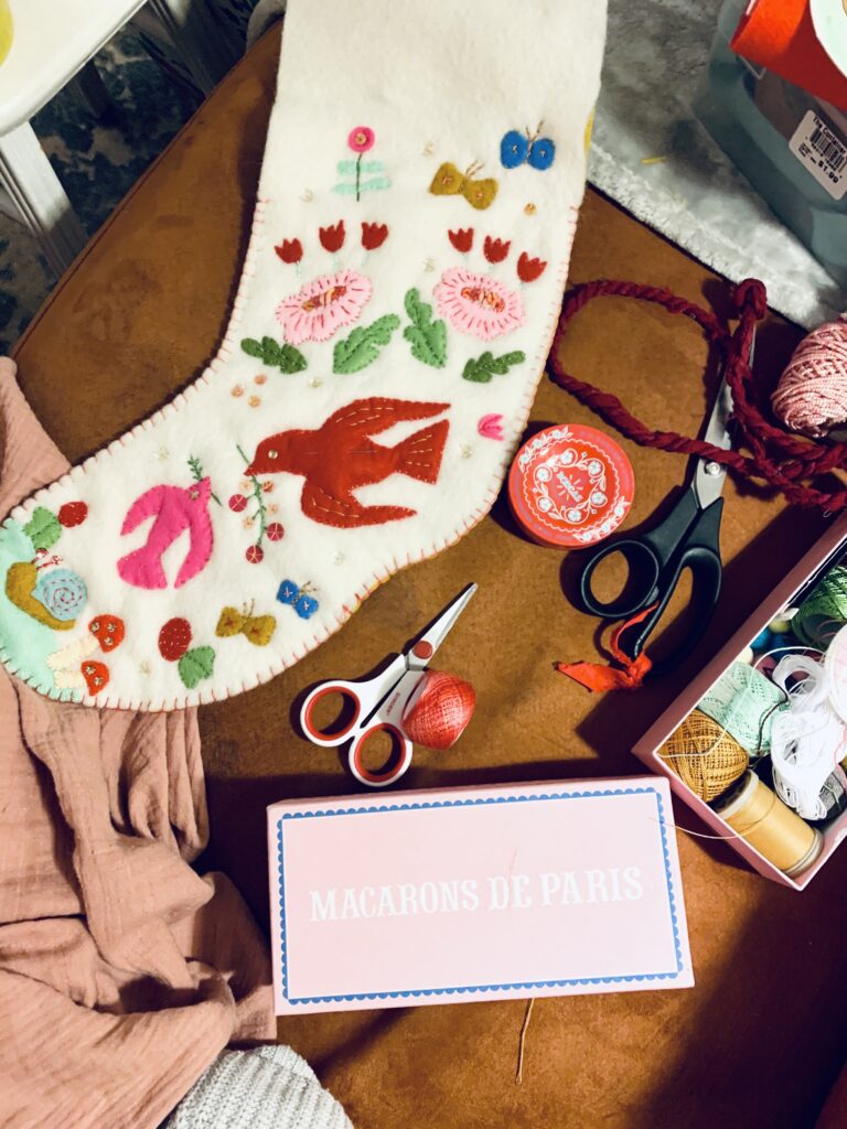 image of handmade heirloom stocking in progress with felt applique surrounded by embroidery supplies like scissors and thread