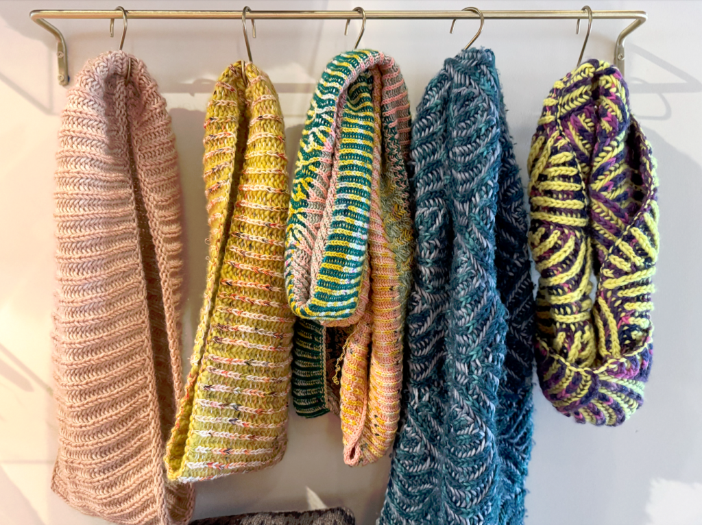 image of many colorful knitted scarves hanging in a line on hangers, illustrating that knitting is meditative and requires focus
