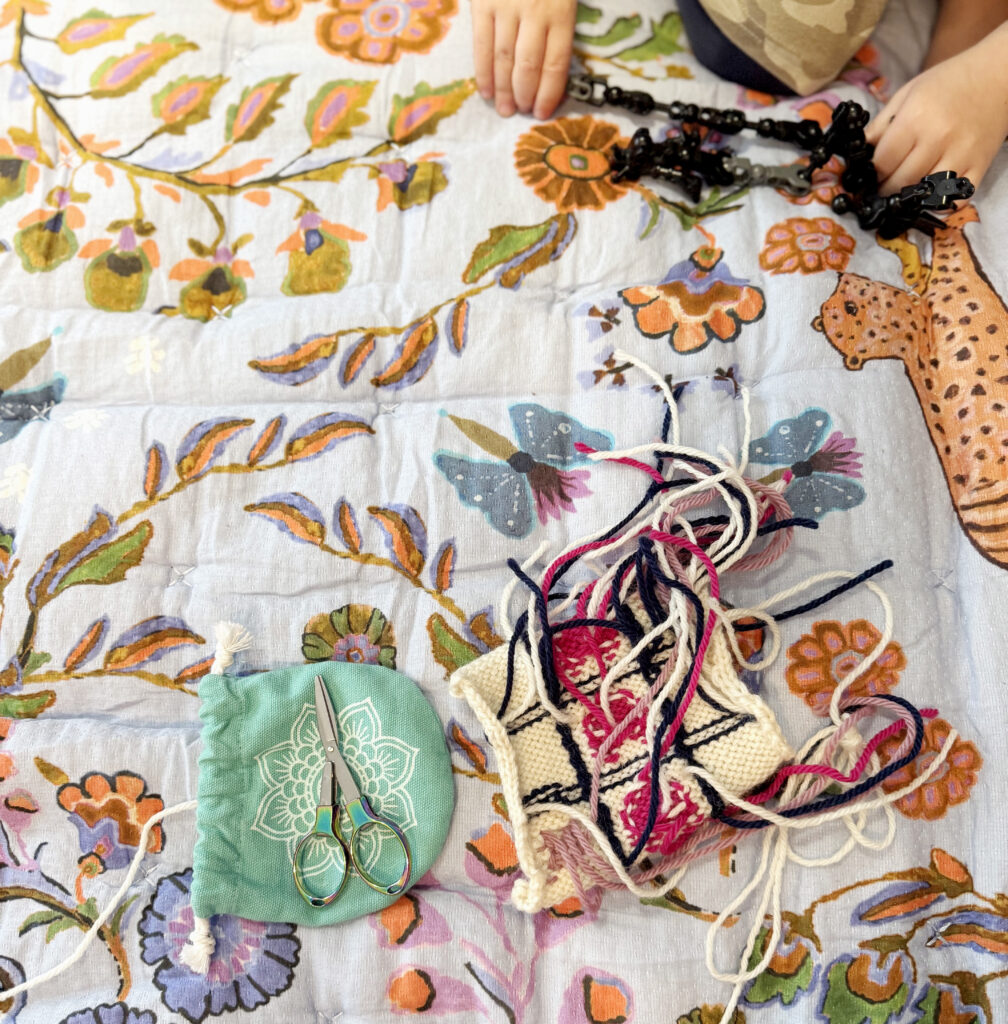 image of a floral quilt with part of of a knitting project and some knitting tools on it to illustrate taking time to knit for self-care