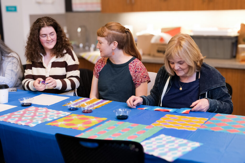 image of three people sitting at table with a blue table cloth, dyeing paper with a Japanese method called orizomegami.