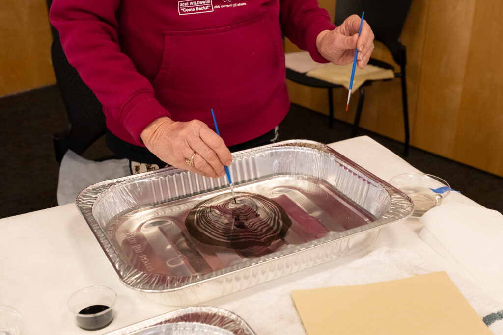 image of someone using one small brush in each hand to create a marbling effect with black on water in a large tin